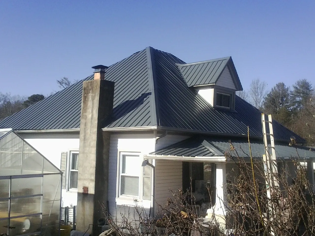 Dark blue standing seam metal roof on a white farmhouse with dormer — Slate & Tile Roof Repair by Roofing Brothers in Lake Lure