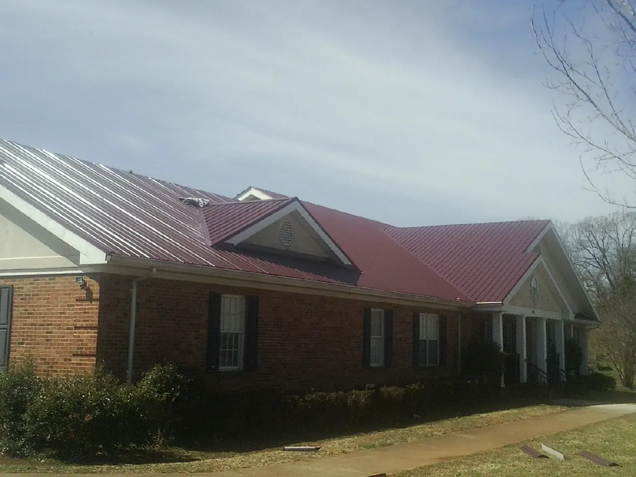 Red metal roof with gabled entries on a long brick building, from a Hail Damage Roof Repair job in Lake Lure