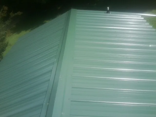 New green metal panels meeting at the ridge of a roof — Flat Roof Repair work by our crew in Lake Lure