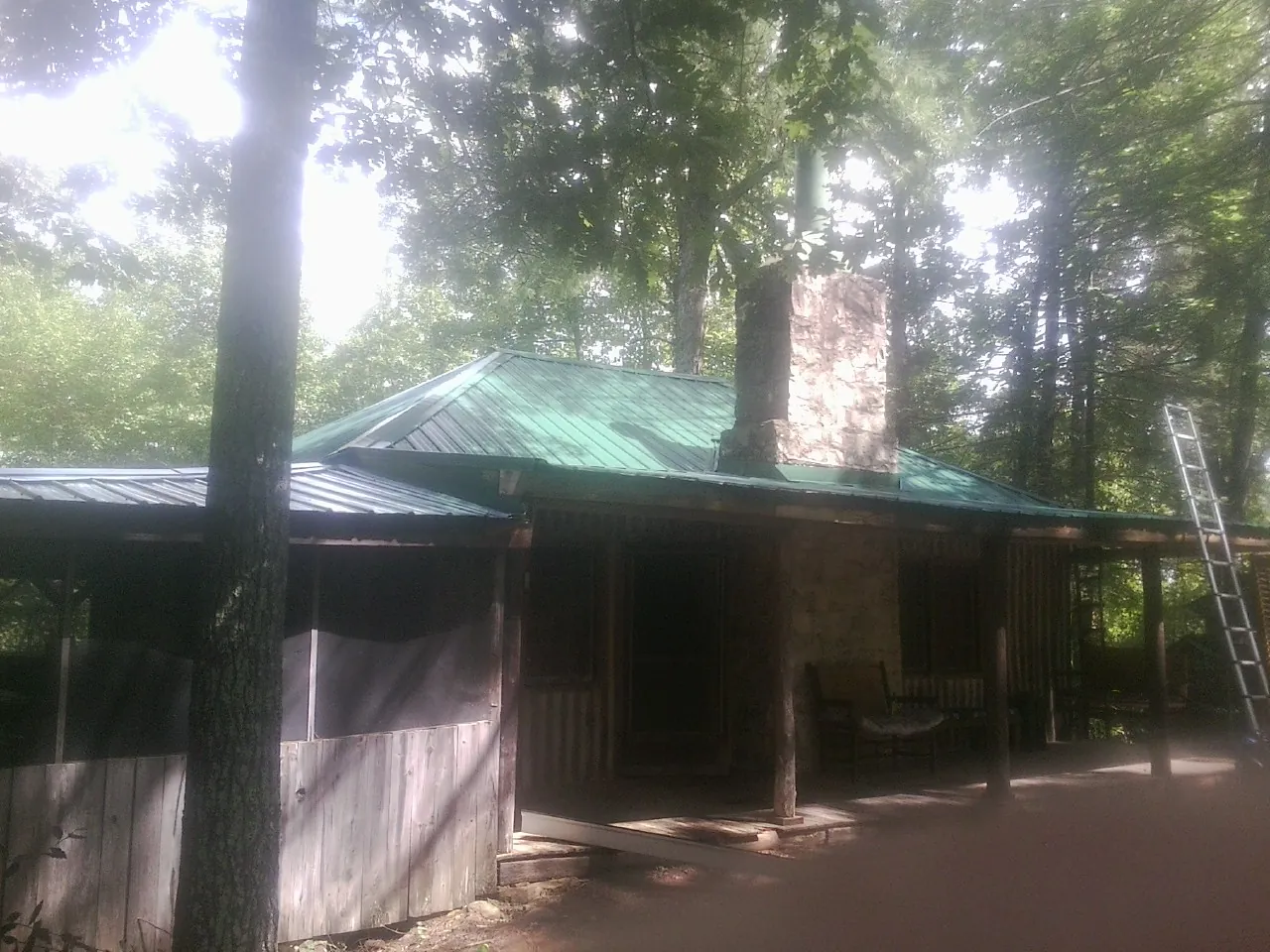 Green metal roof and stone chimney above a log cabin porch in Lake Lure