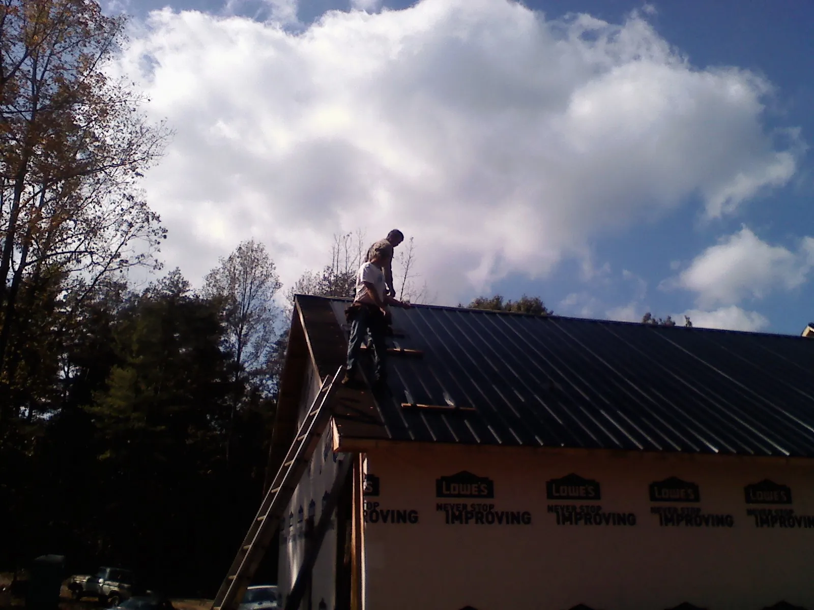 Roofer fastening dark metal panels high against a cloudy sky, from a Roof Inspection job in Lake Lure