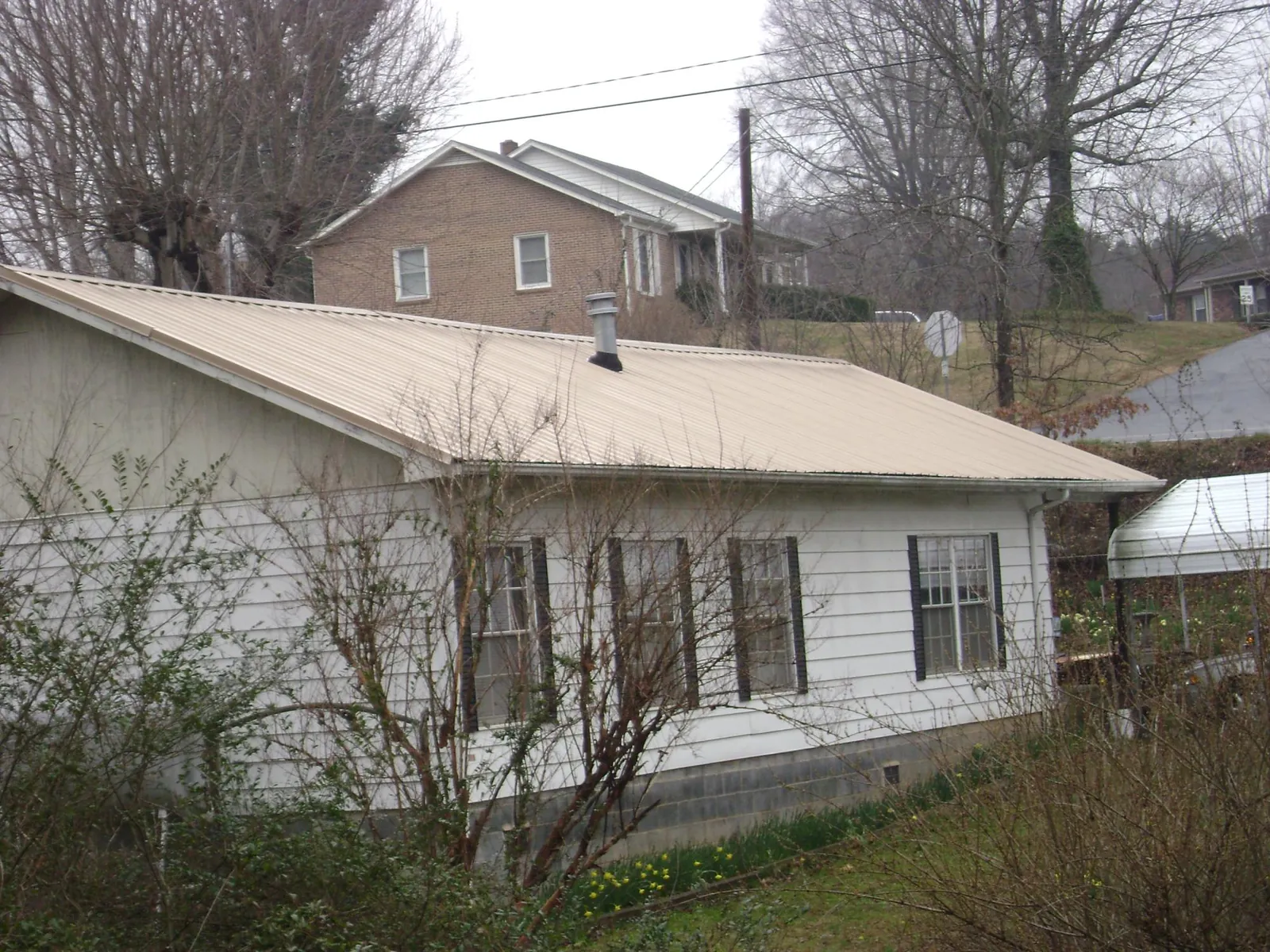 Tan metal roof on a white sided house set into a hillside — Commercial Roofing by Roofing Brothers in Lake Lure