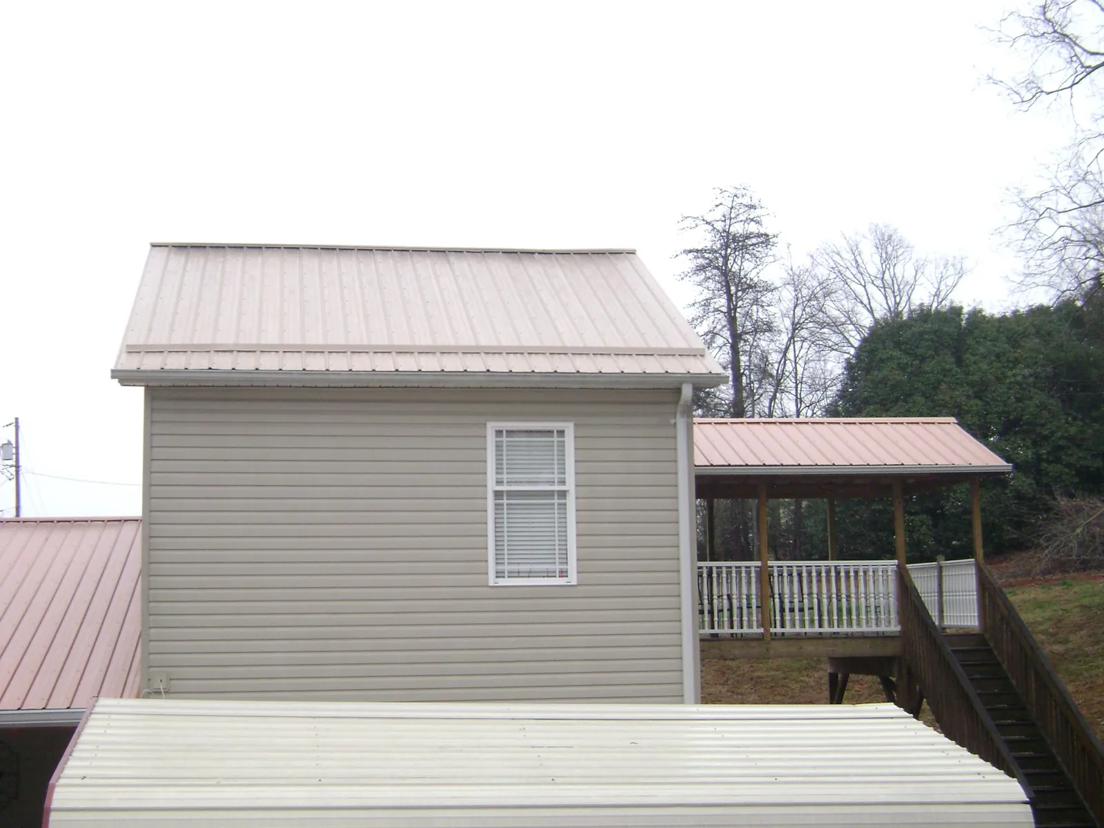 Tan metal roofs on a two story addition and attached porch, from a Roof Replacement job in Lake Lure
